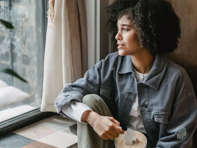 Mujer pensativa con una taza junto a la ventana, preguntándose si lo que siente es ansiedad o depresión
