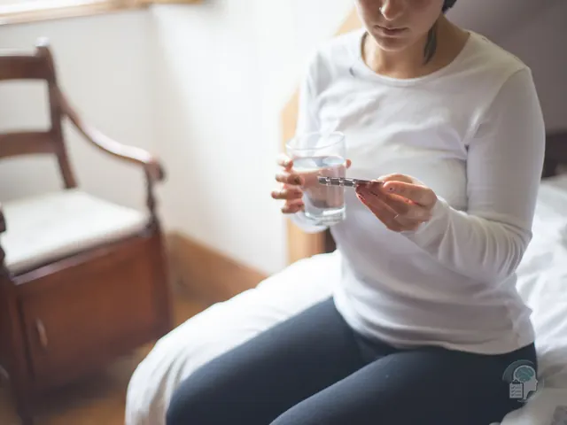Mujer sentada en la cama con un vaso de agua y un blíster de ansiolíticos en la mano