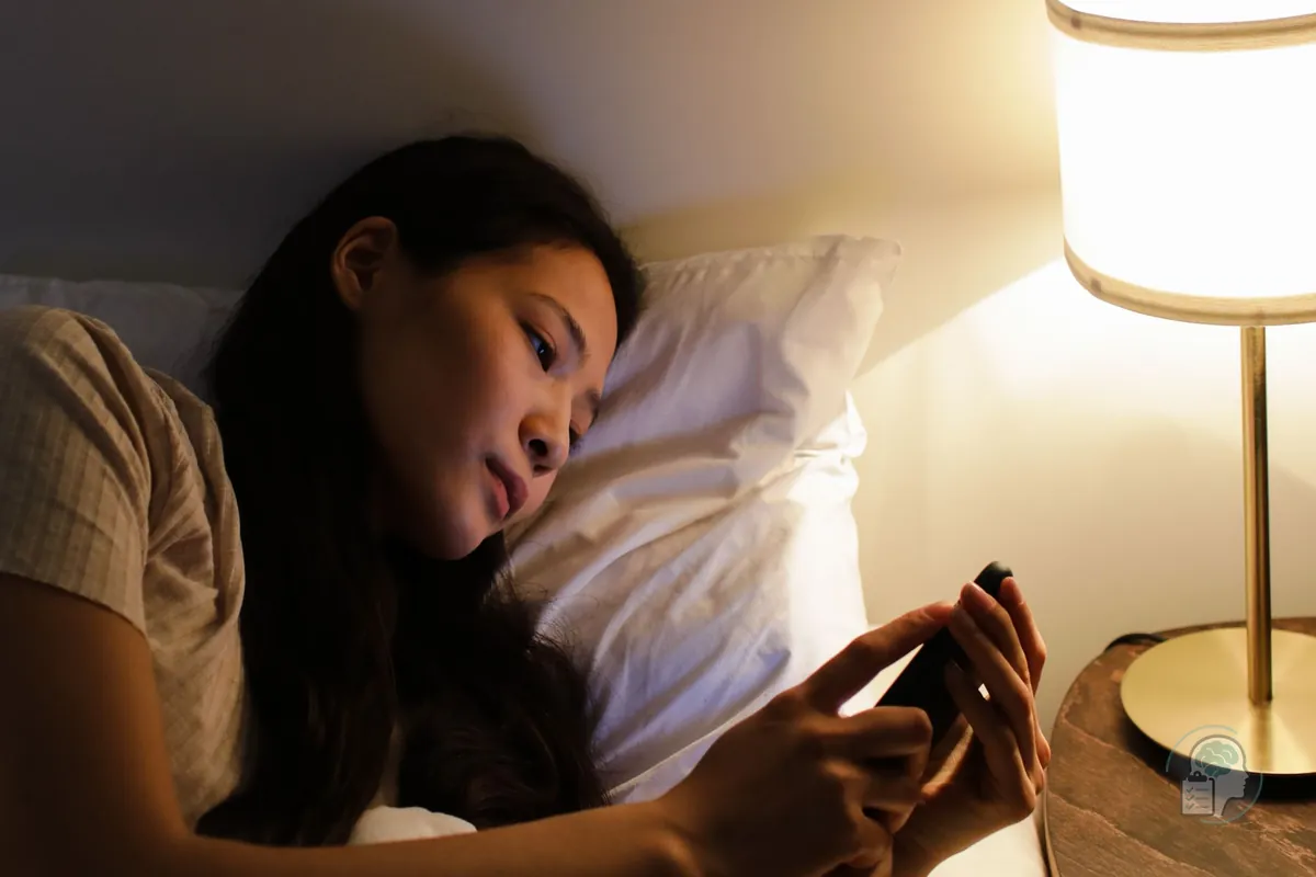 Mujer tumbada en la cama de noche mirando el móvil a la espera de un mensaje, una escena típica del apego ansioso