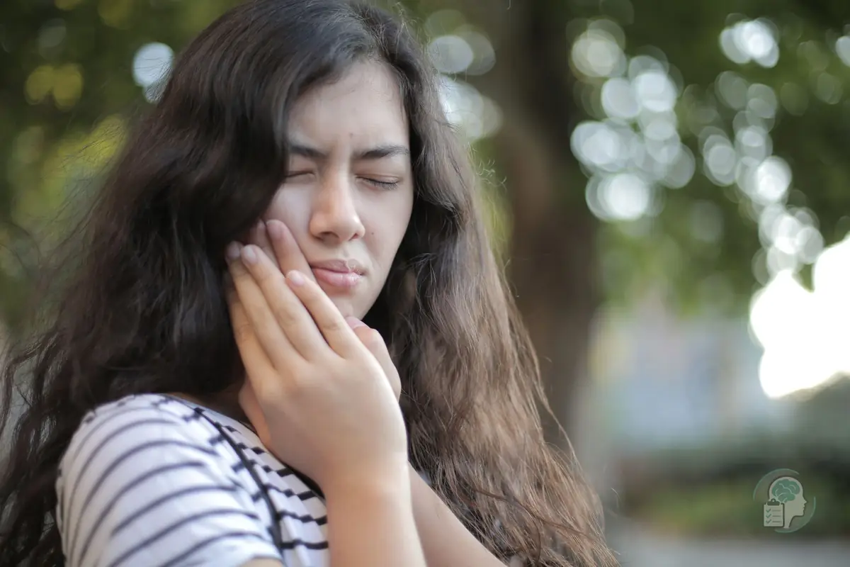 Mujer joven con los ojos cerrados que se sujeta la mandíbula con gesto de dolor, una imagen del bruxismo por estrés