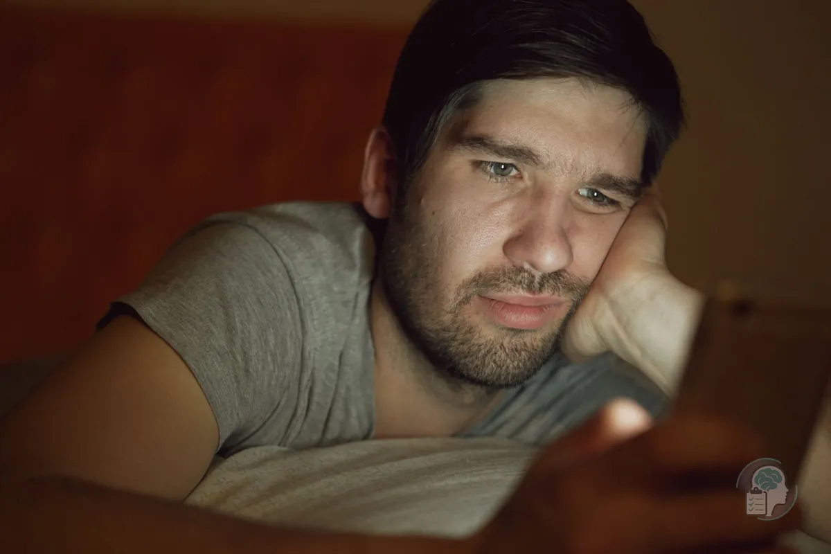 Hombre tumbado en la cama de noche que mira el móvil con gesto abatido, una imagen de compararse con los demás en las redes sociales