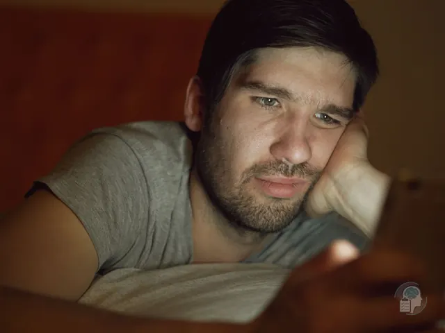 Hombre tumbado en la cama de noche que mira el móvil con gesto abatido, una imagen de compararse con los demás en las redes sociales