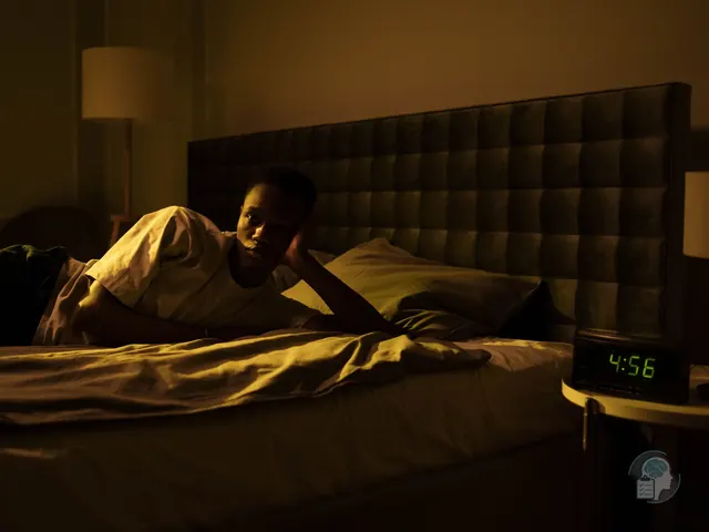 Hombre despierto en la cama de madrugada junto a un despertador que marca las 4:56, una imagen del despertar precoz