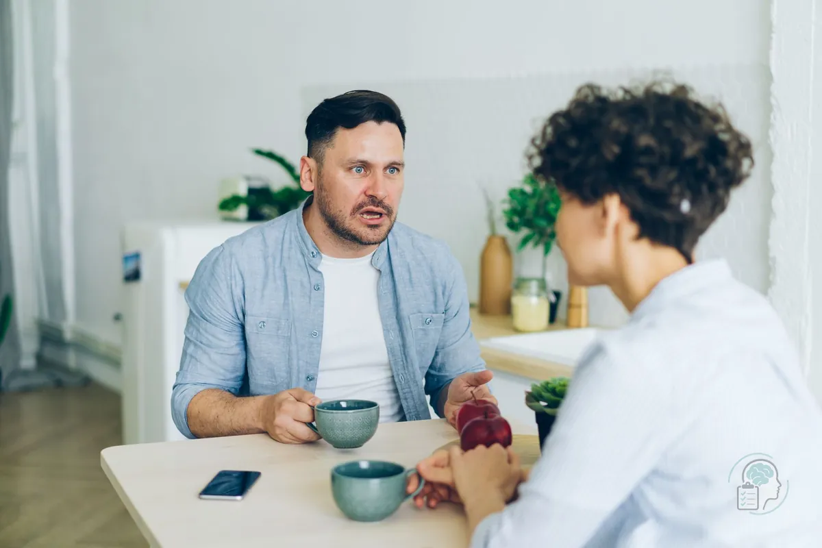 Pareja hablando en serio en la mesa de la cocina con el móvil apartado, una forma de afrontar los celos en la pareja sin reproches