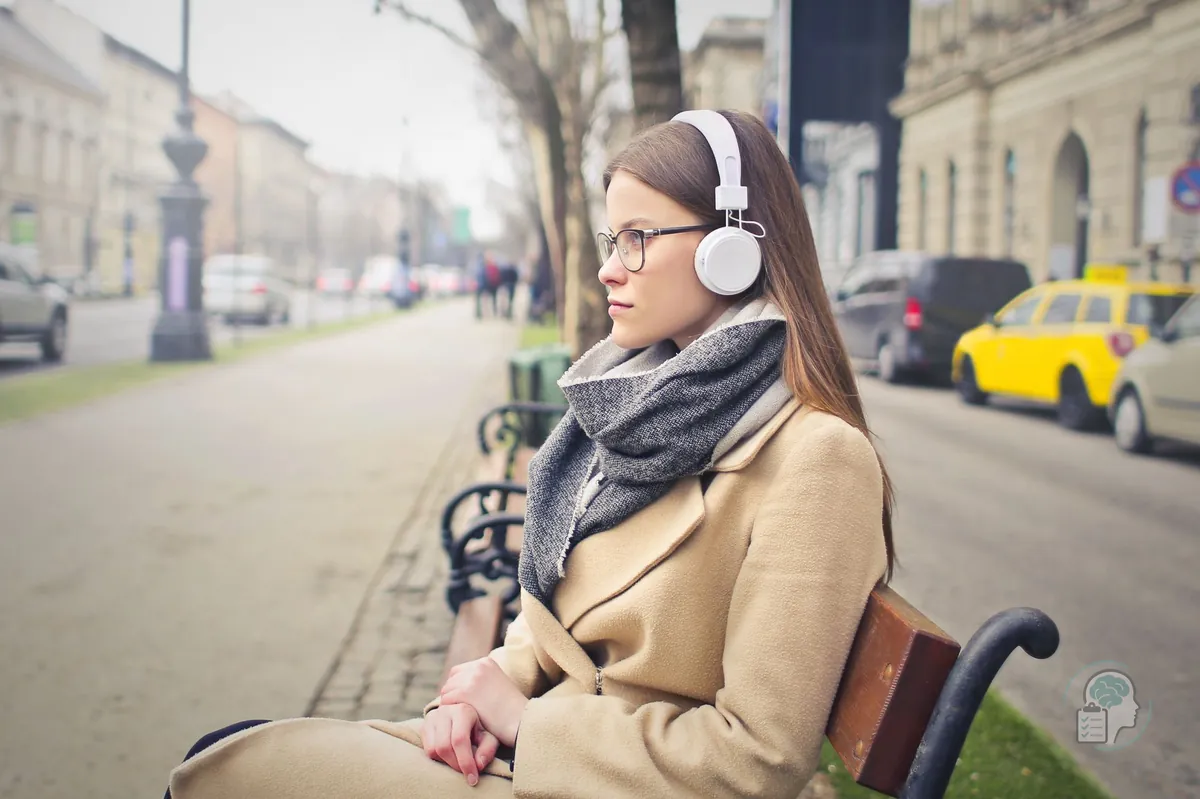Adult woman wearing headphones sitting on a street bench managing her sensory environment