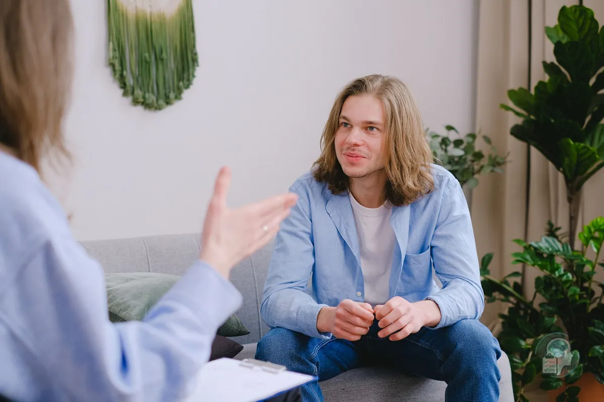 Jove adult conversant tranquil amb la seva psicòloga en una sessió de teràpia adaptada per a adults autistes