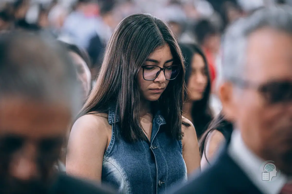 Joven con gafas que baja la mirada en medio de una multitud, una imagen de la ansiedad social