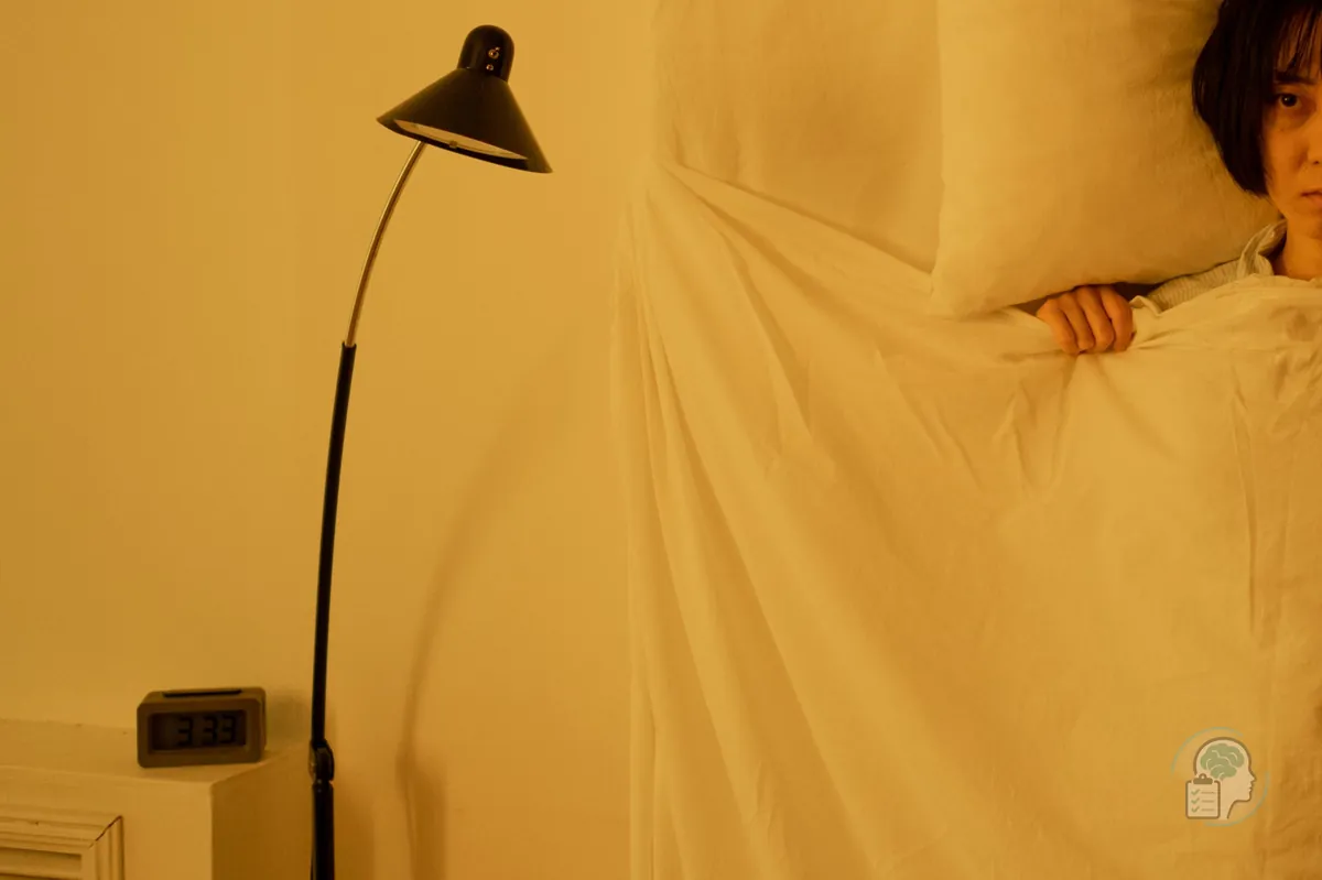 Mujer despierta de madrugada que se asoma bajo la sábana junto a un reloj que marca las 3:33, una escena típica del insomnio