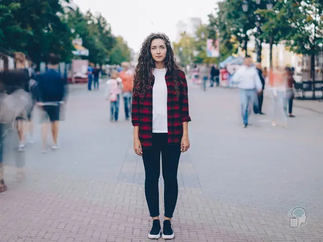 Mujer joven quieta en mitad de una calle peatonal mientras la gente pasa desenfocada a su alrededor, una imagen de sentirse diferente a los demás