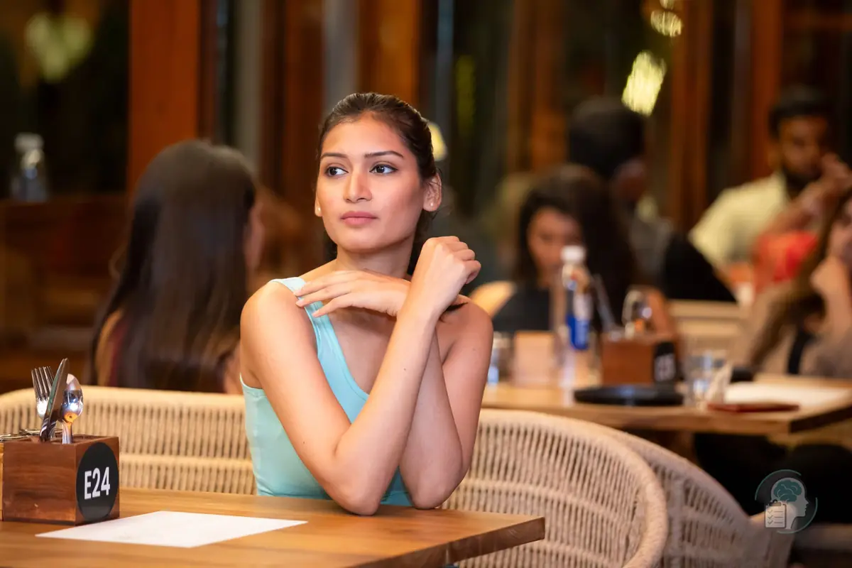 Mujer joven pensativa, sola en su mesa de un restaurante lleno de gente que charla detrás de ella, una imagen de sentirse diferente entre los demás