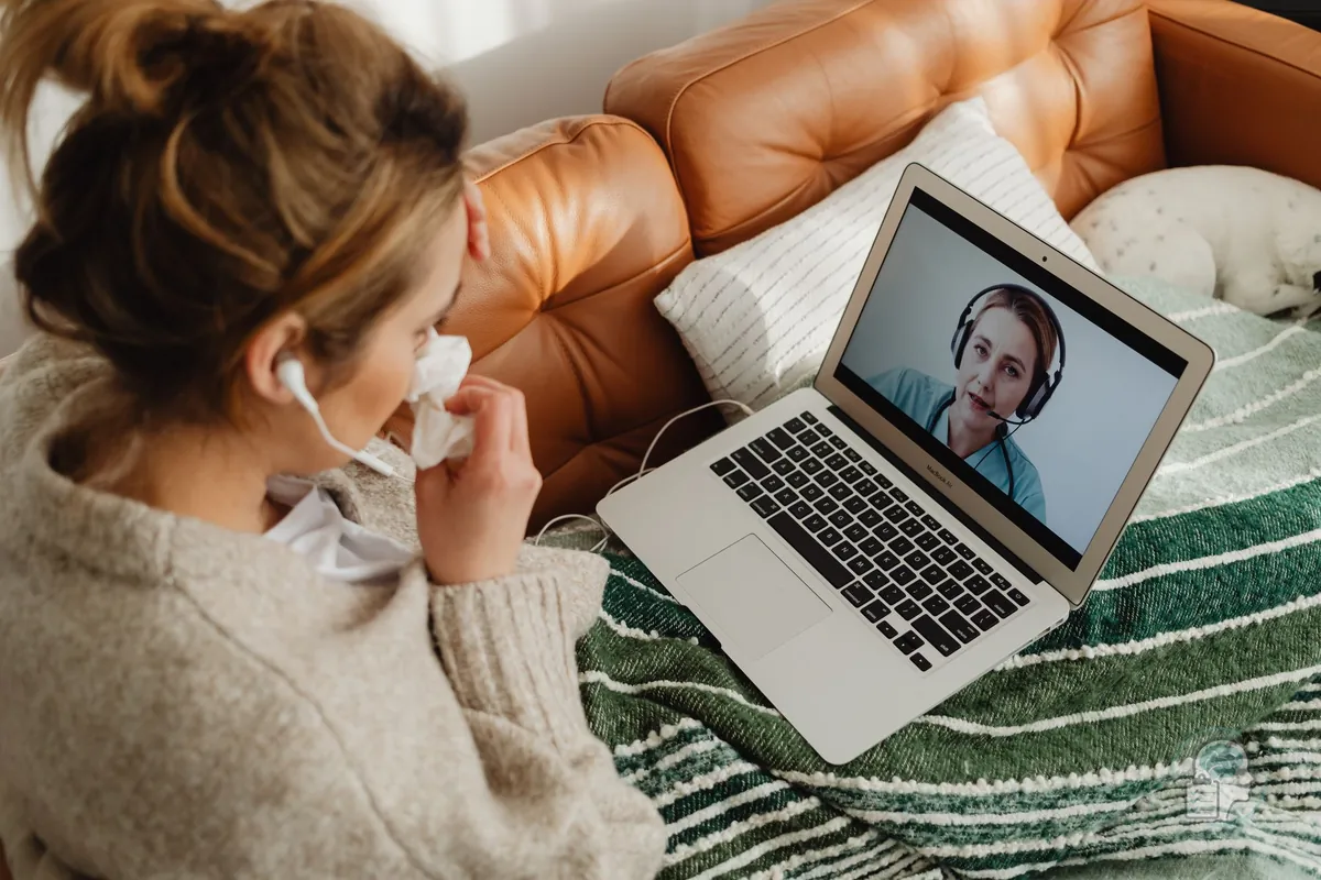 Mujer siguiendo una sesión de terapia online desde el sofá de su casa con auriculares y portátil