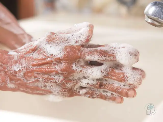 Manos cubiertas de espuma de jabón bajo el grifo, el lavado repetido típico del TOC de limpieza