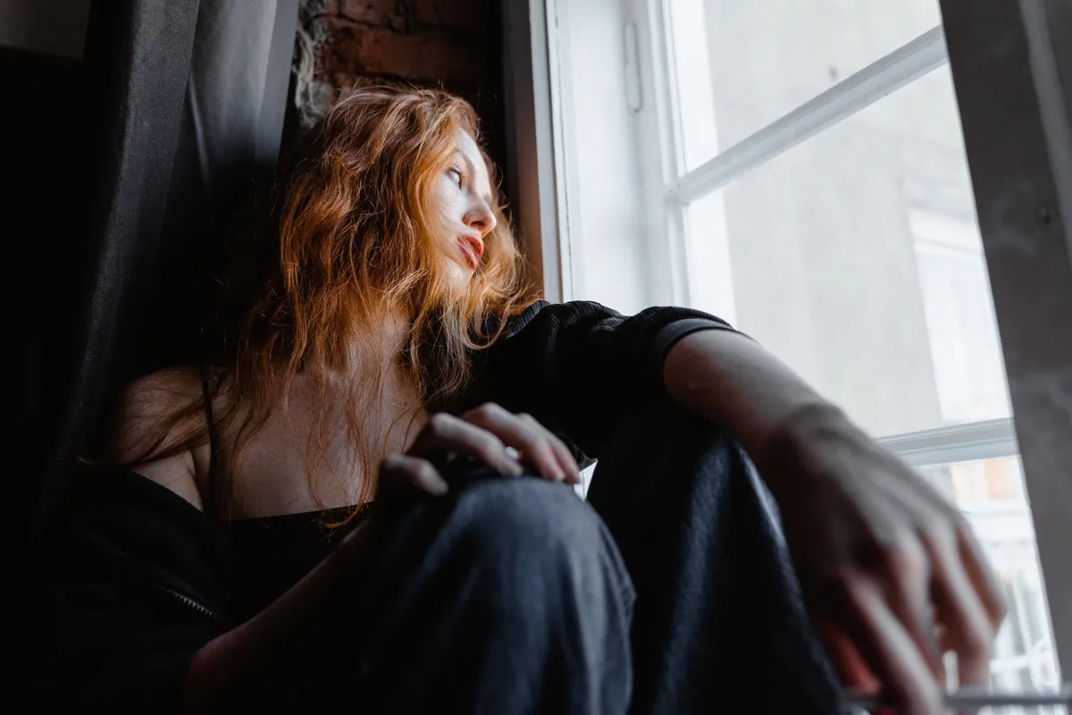 Mujer pensativa sentada junto a una ventana, ilustrando la preocupación y la tensión que mide el test de ansiedad