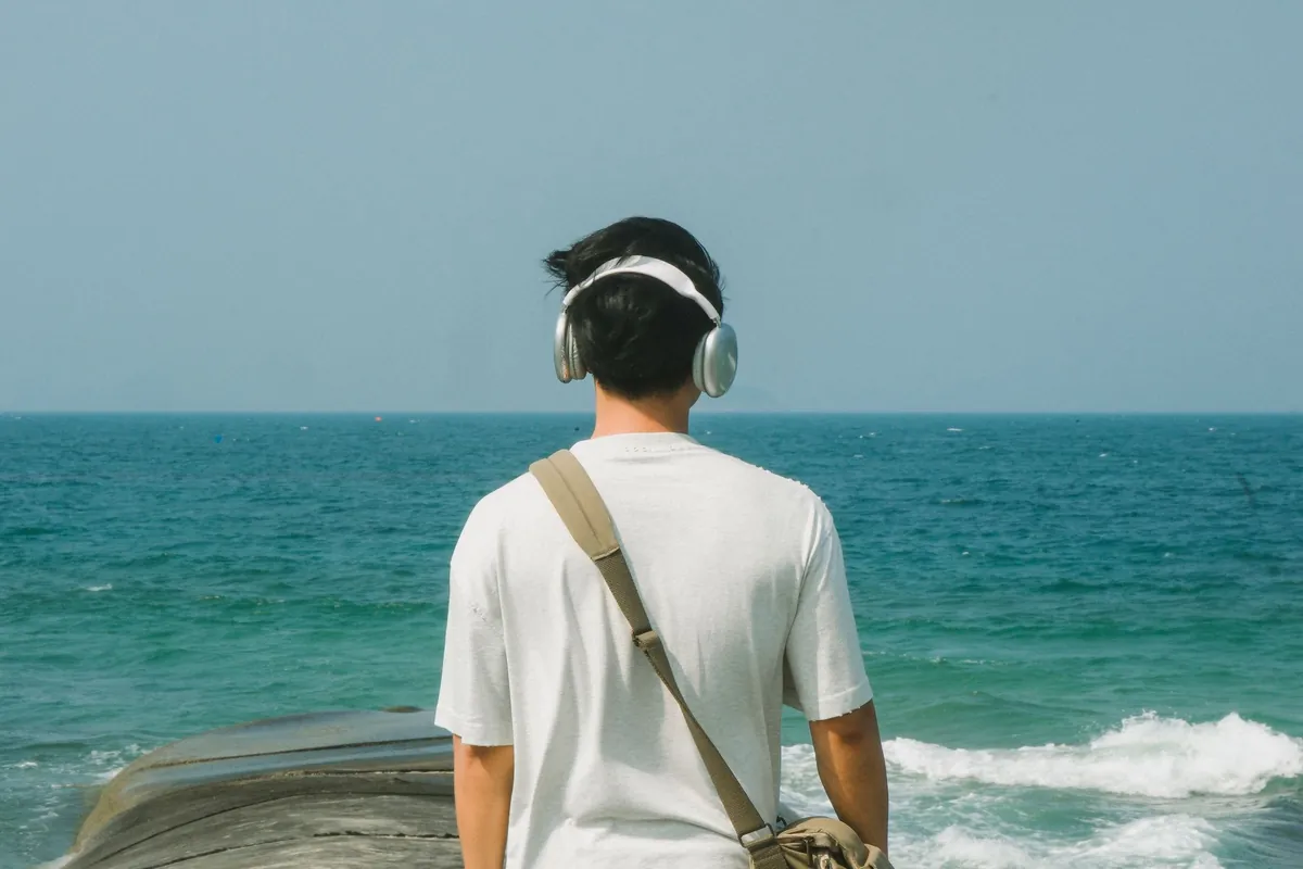 Joven con auriculares mirando el mar en calma, en busca de un entorno tranquilo; imagen del test de autismo en adultos