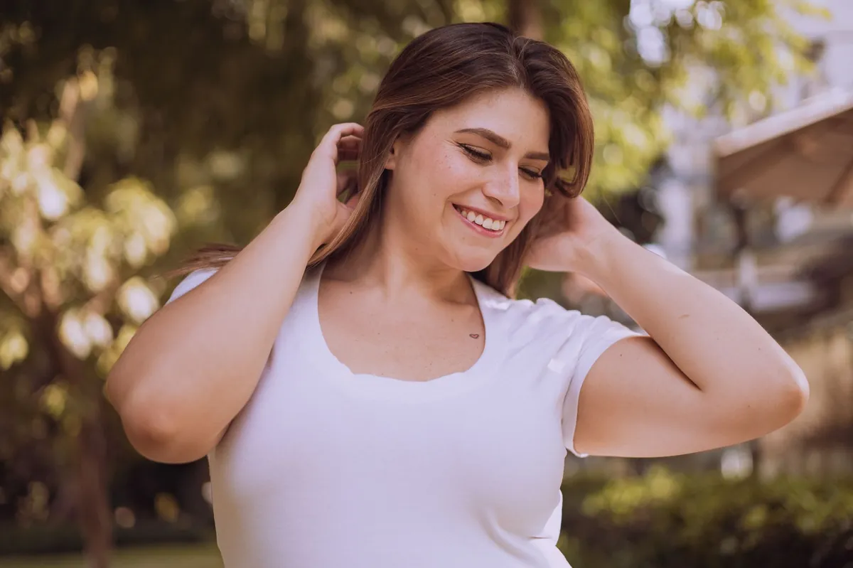 Mujer sonriendo al aire libre con las manos en el pelo, ilustrando la confianza y el bienestar que mide el test de autoestima