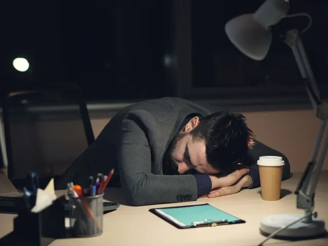 Persona dormida sobre el escritorio de noche con la lámpara encendida, imagen del agotamiento que mide este test de burnout