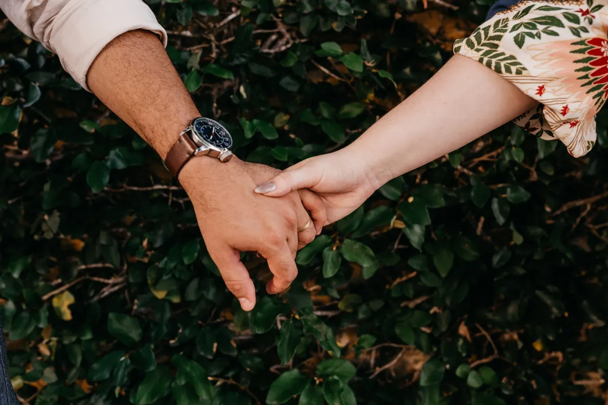 Pareja cogida de la mano sobre un seto verde, ilustrando el vínculo afectivo que explora el test de dependencia emocional