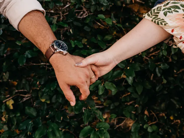 Pareja cogida de la mano sobre un seto verde, ilustrando el vínculo afectivo que explora el test de dependencia emocional