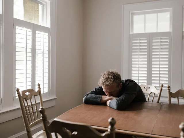 Persona con la cabeza apoyada sobre una mesa junto a unas ventanas luminosas, ilustrando el desánimo que valora el test de depresión