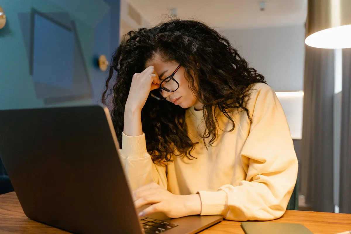 Mujer agotada con la mano en la cabeza frente al portátil de noche, ilustrando el estrés acumulado que evalúa este test de estrés