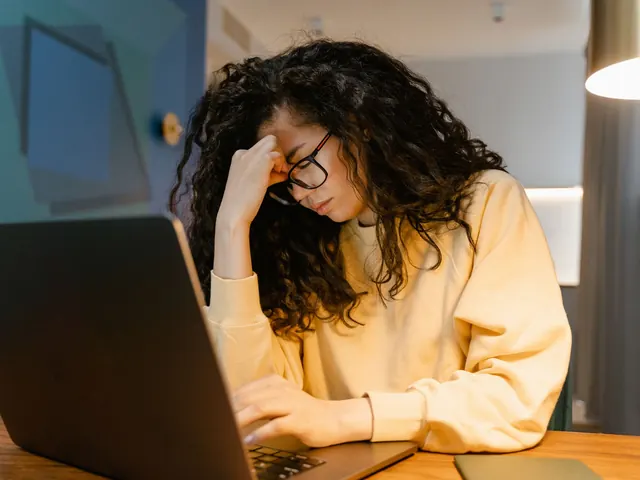 Mujer agotada con la mano en la cabeza frente al portátil de noche, ilustrando el estrés acumulado que evalúa este test de estrés
