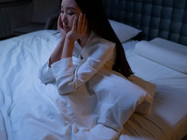Mujer sentada en la cama de noche con las manos en la cara, sin poder dormir, ilustrando los síntomas del insomnio que valora este test