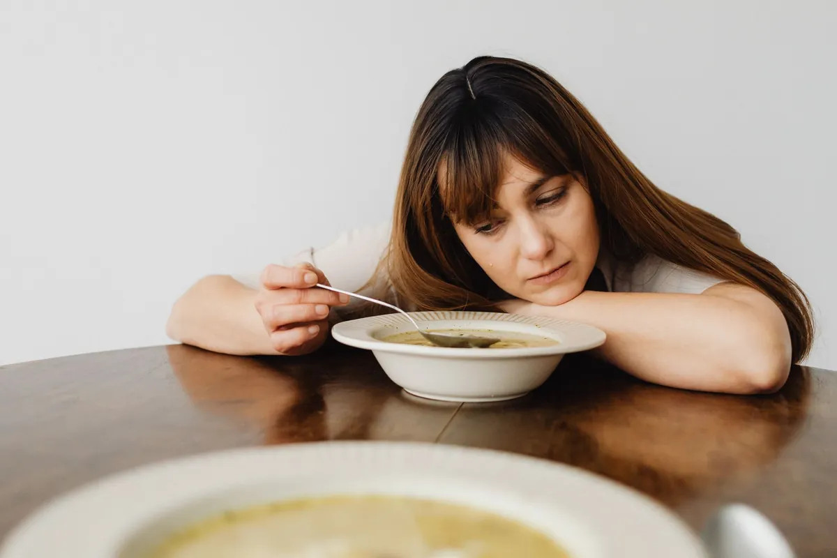 Mujer mirando abatida un plato de sopa sobre la mesa, ilustrando la relación difícil con la comida propia de los trastornos alimentarios (TCA)